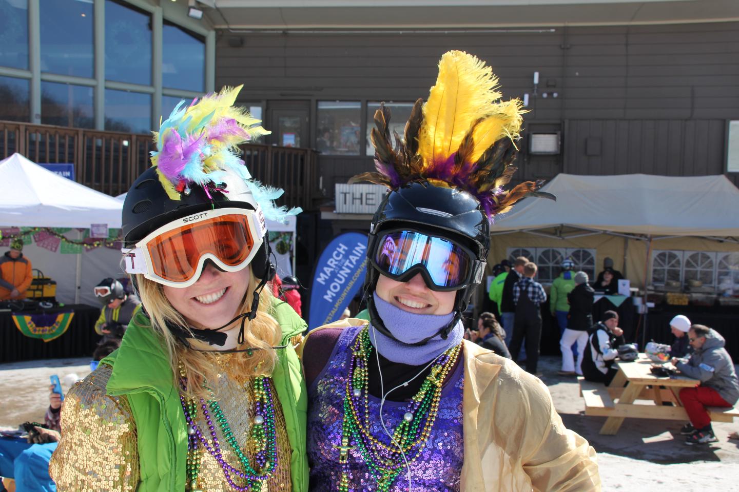 Friends in festive attire with feathers and beads, smiling outdoors on a sunny day.