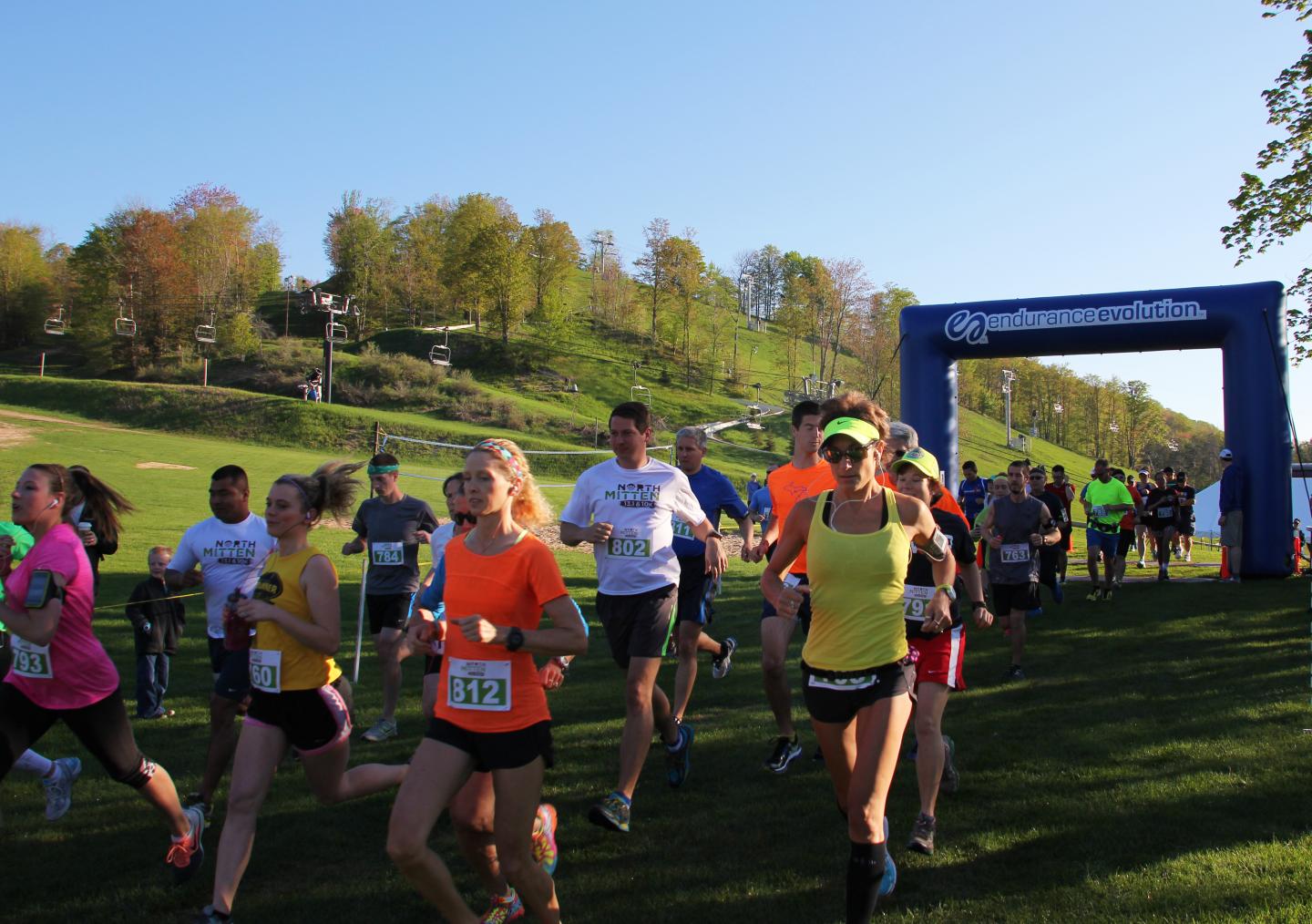 Runners participating in a grassy outdoor race under a blue archway.