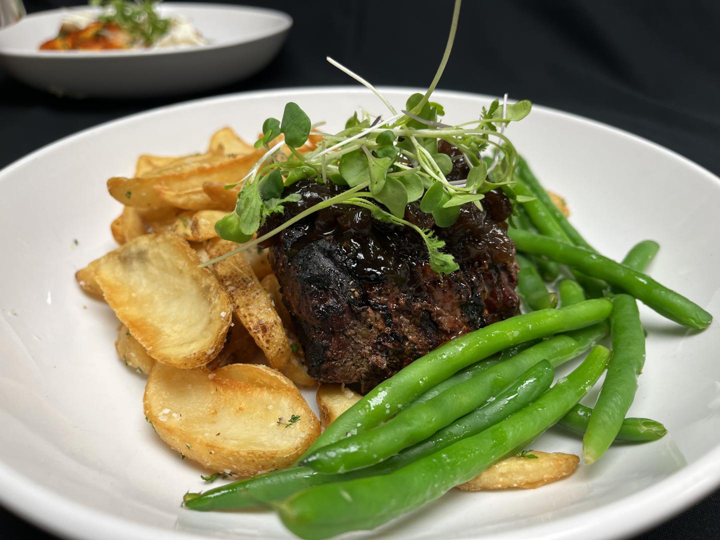 Steak with fries, green beans, and microgreens on a white plate.