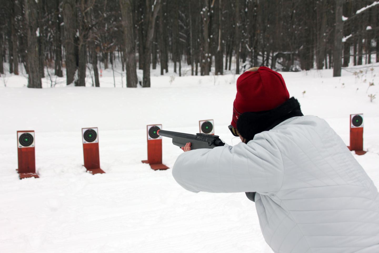 Person aiming a rifle at targets in a snowy forest.