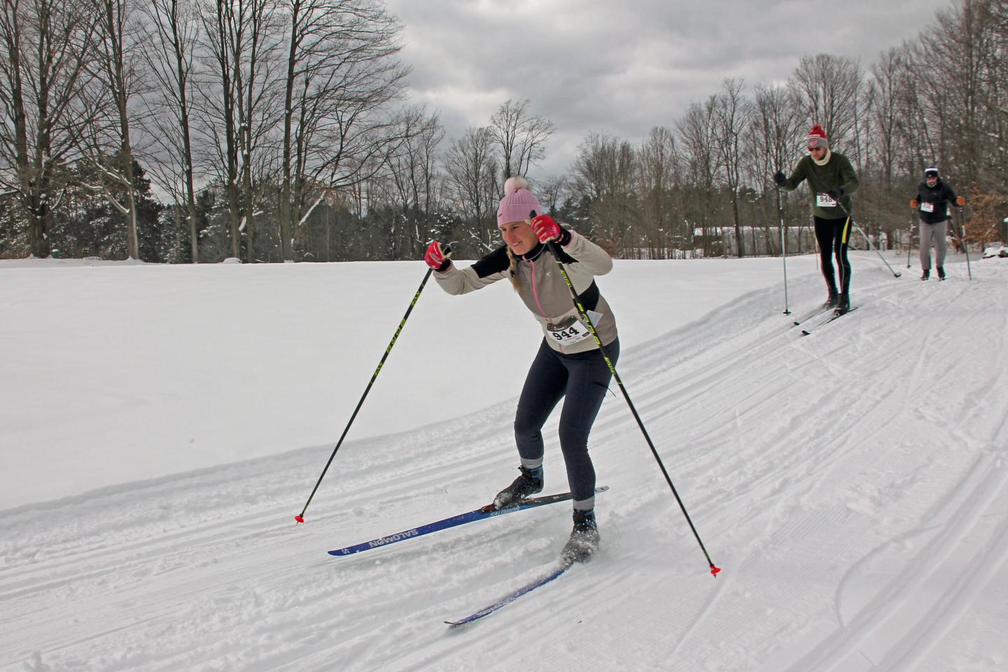 Skiers cross-country skiing on a snowy trail, winter landscape in the background.