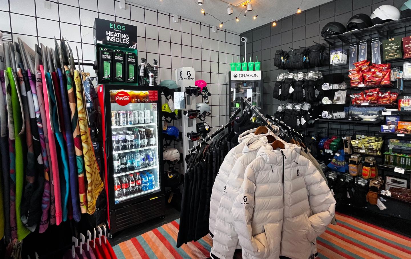 A clothing store with jackets, a drink cooler, and assorted gear on shelves.