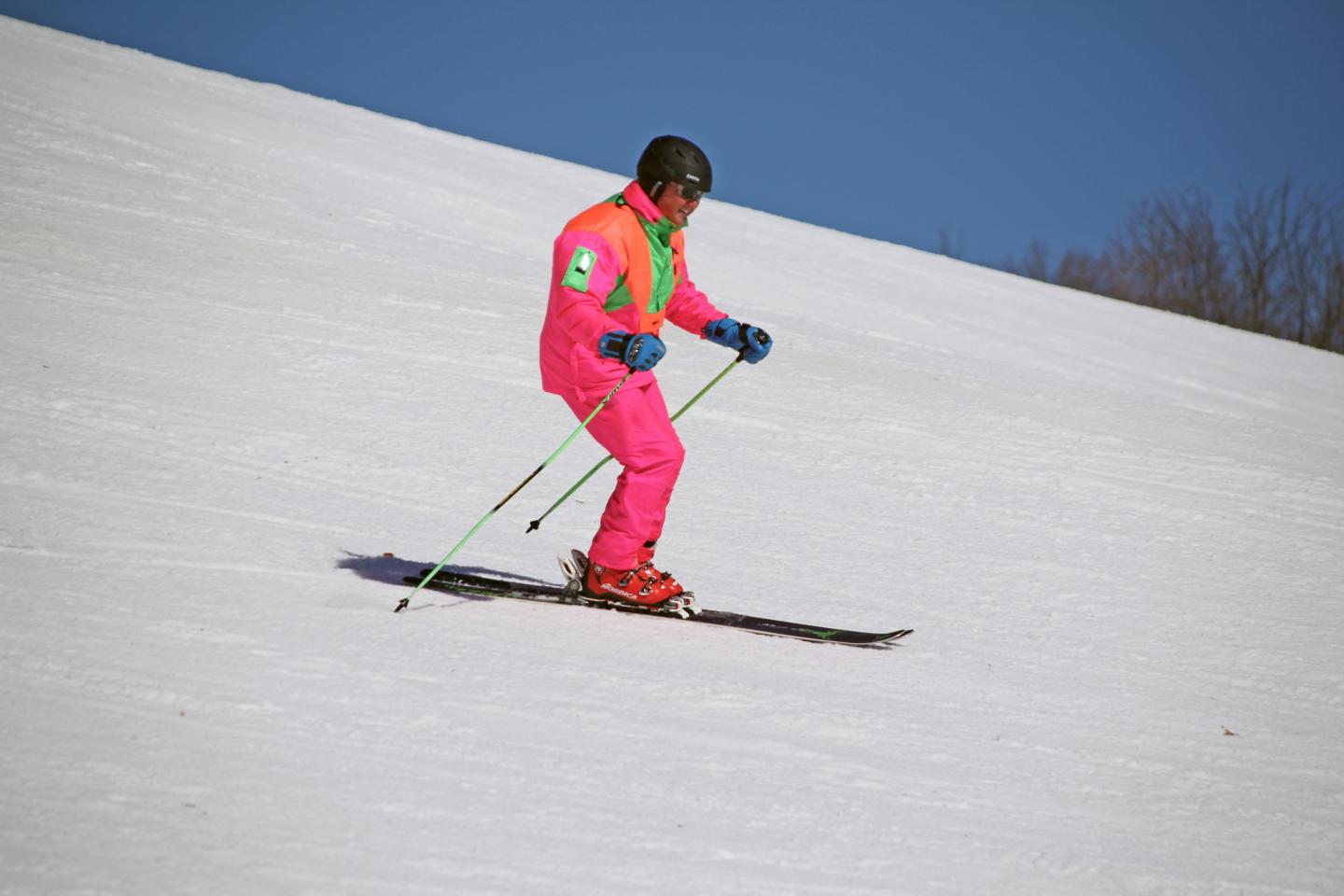 Skier in bright pink gear skiing downhill on a sunny day.