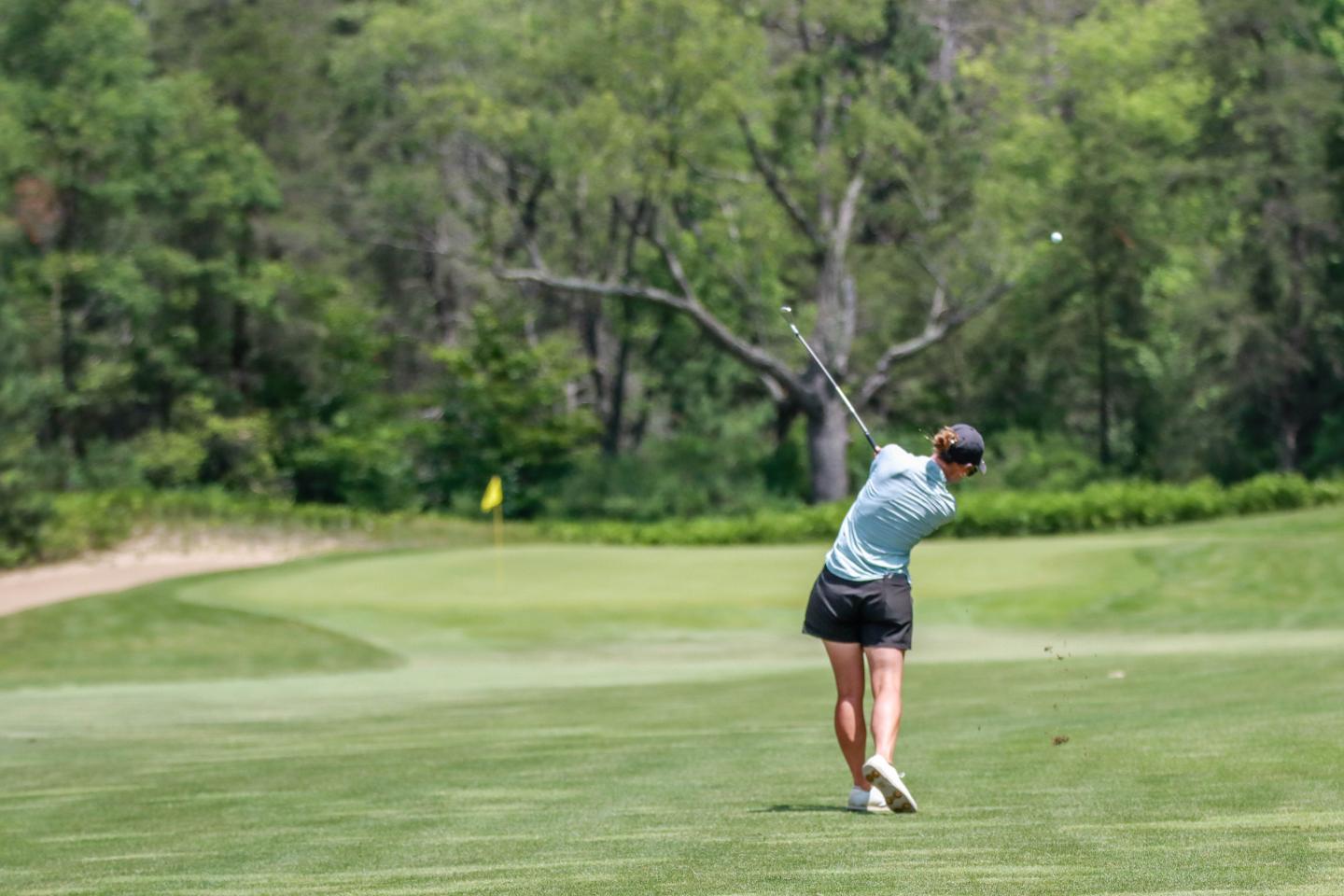 Golfer swinging on a lush, green course surrounded by trees.