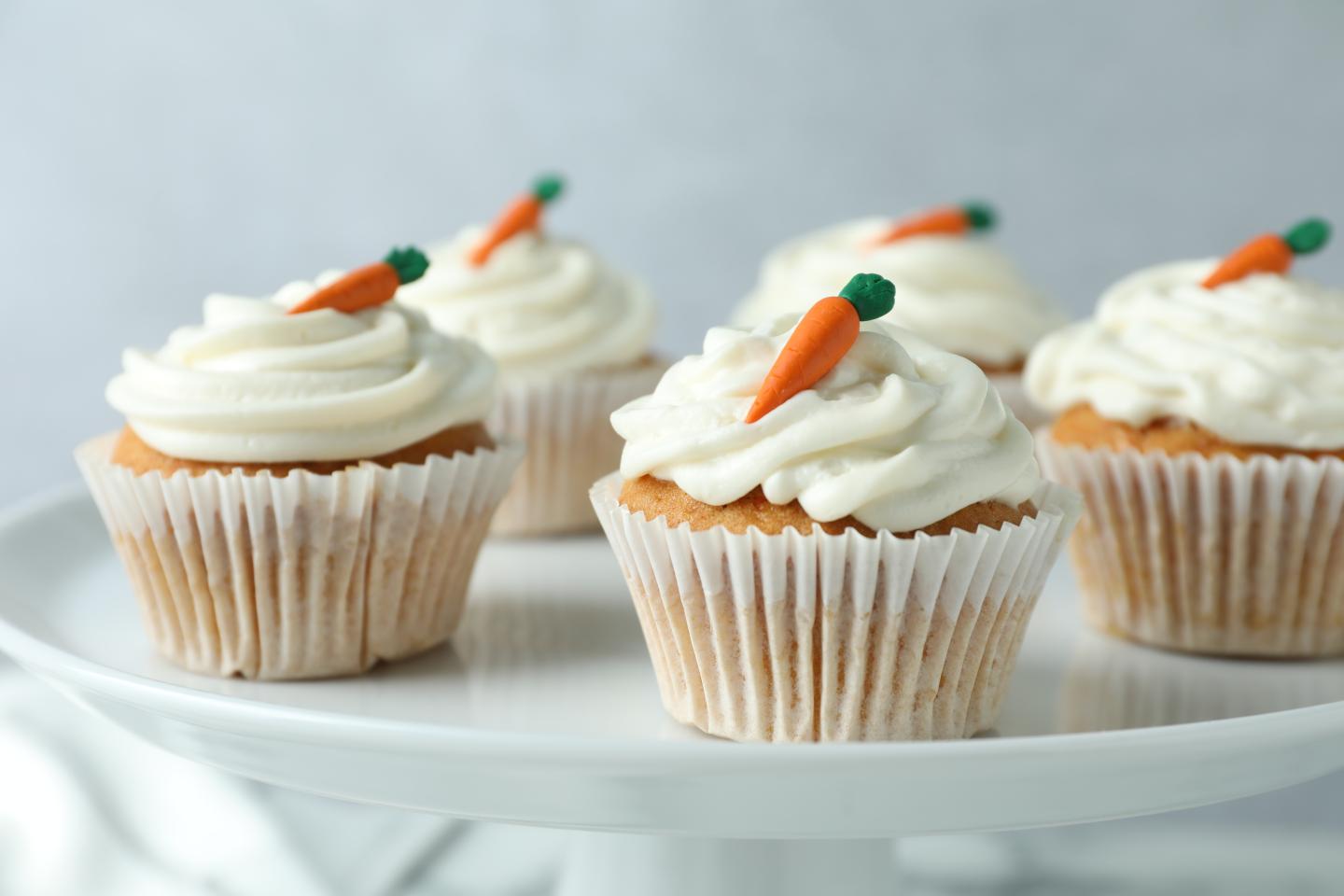 Cupcakes with white frosting and small carrot decorations on top.
