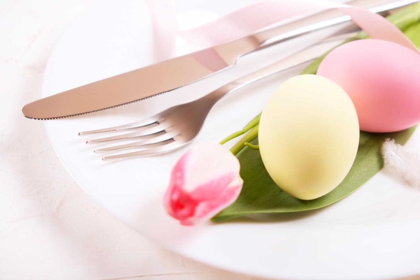Plate with pastel pink and yellow eggs, tulip, and cutlery.