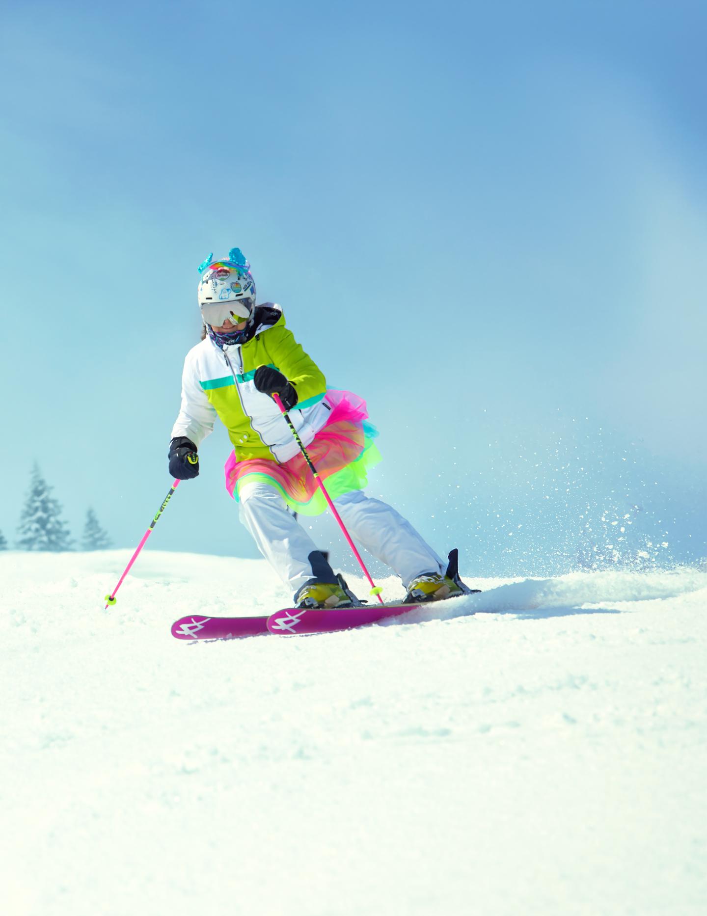Skier in colorful tutu skiing downhill on a sunny day.
