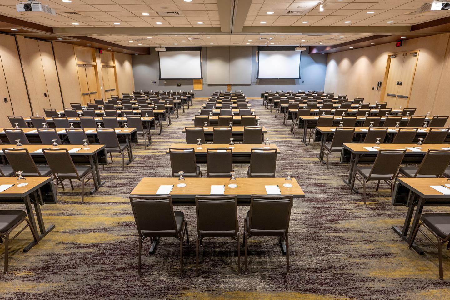 Large conference room with rows of tables and chairs facing two screens.