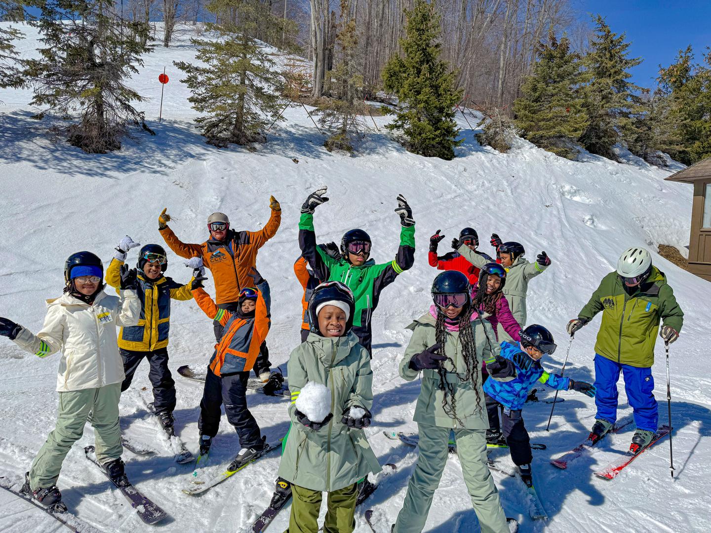Group of skiers posing joyfully on a snowy slope, with trees in the background.