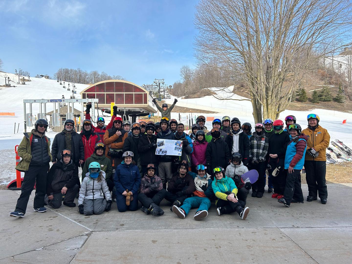 Large group posing outdoors in ski gear at snowy resort.