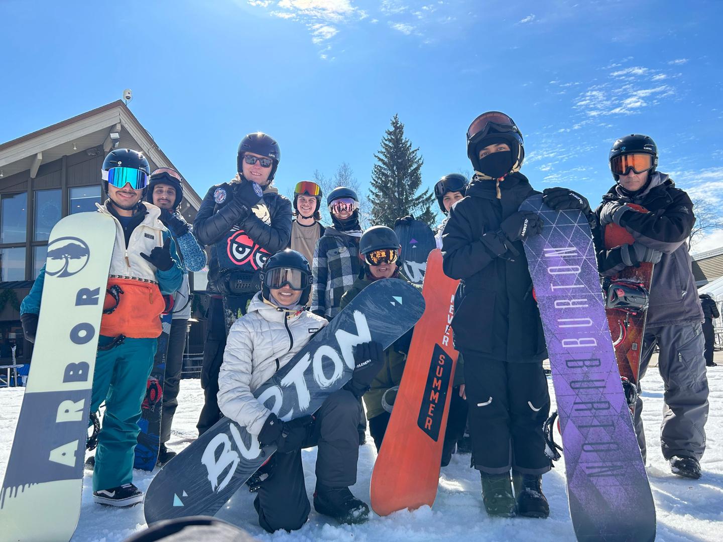 Snowboarders posing in front of a lodge on a sunny day.