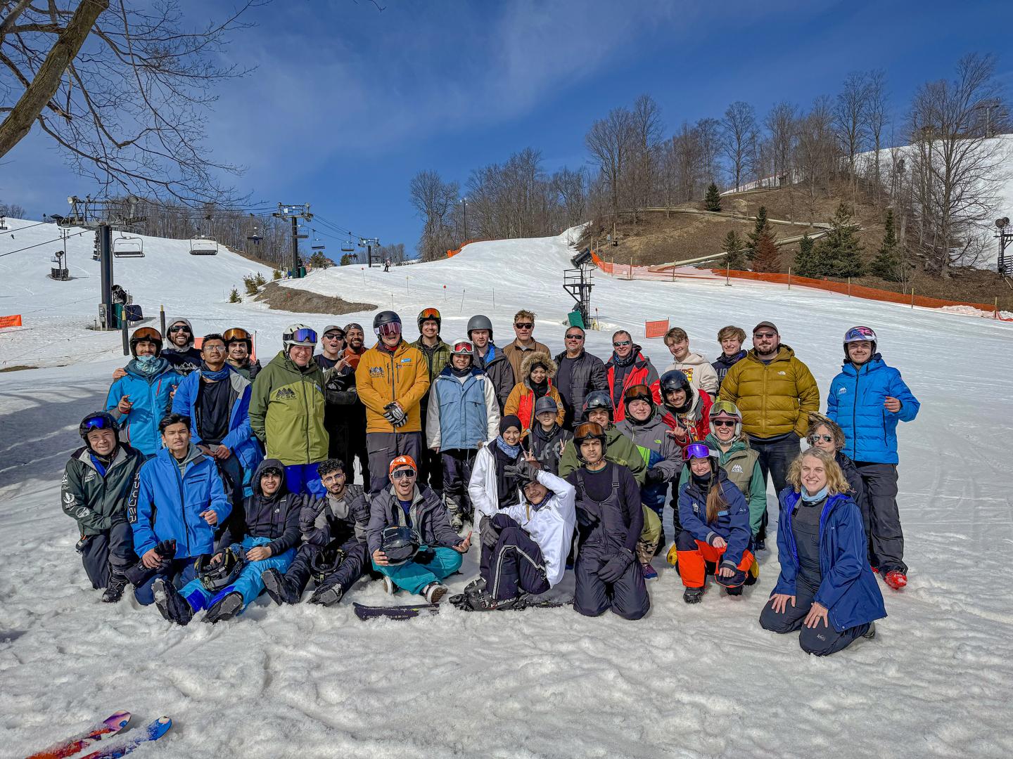 Group of people in winter clothing posing on a snowy ski slope under a blue sky.