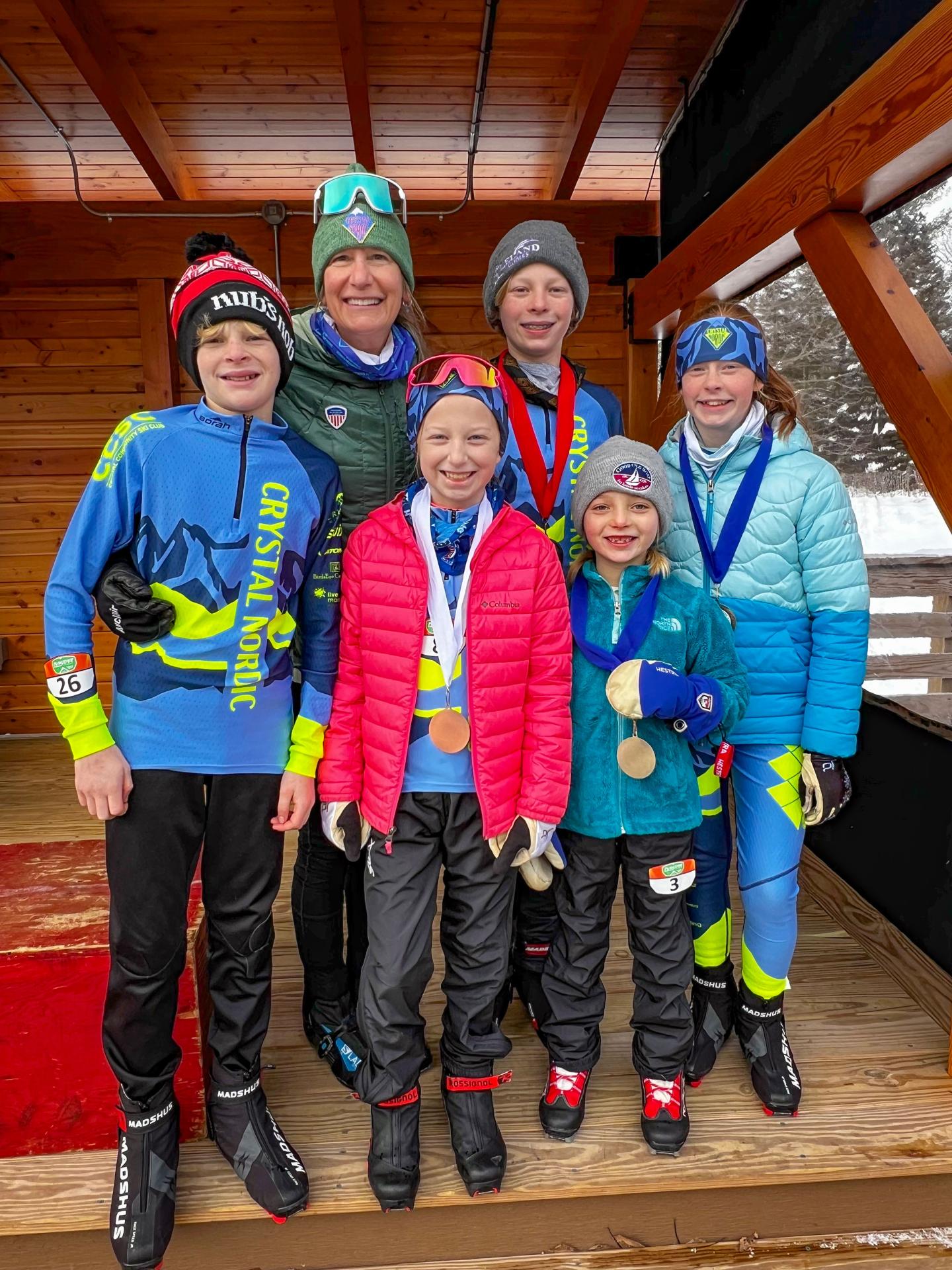 Group of smiling skiers in colorful gear with medals in a wooden lodge setting.