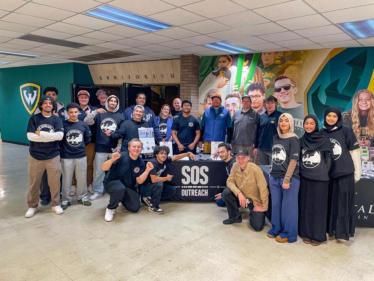 Group of people gathered around an SOS Outreach banner indoors.