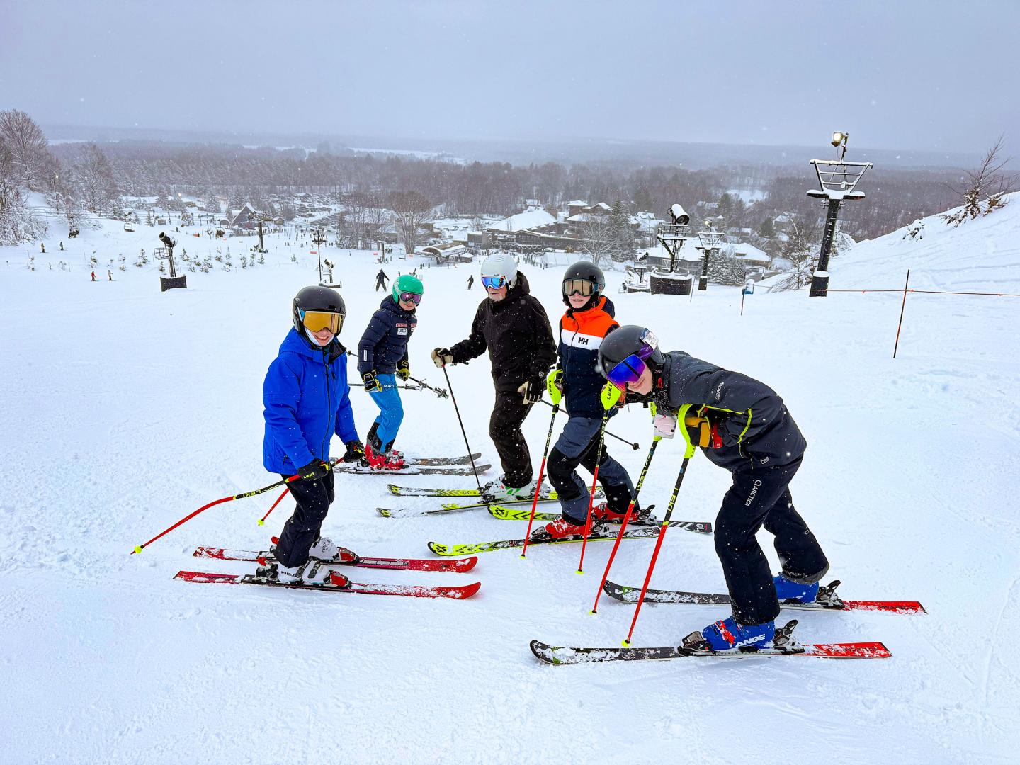 Skiers in colorful gear on a snowy slope, with a snowy landscape in the background.