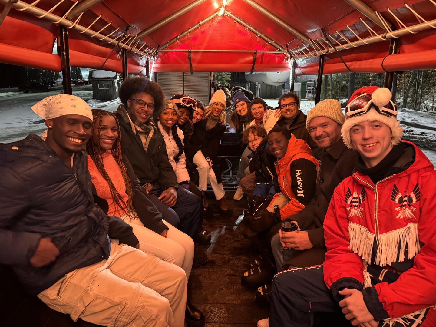 Group of people sitting in a festive, red-roofed wagon, smiling warmly.