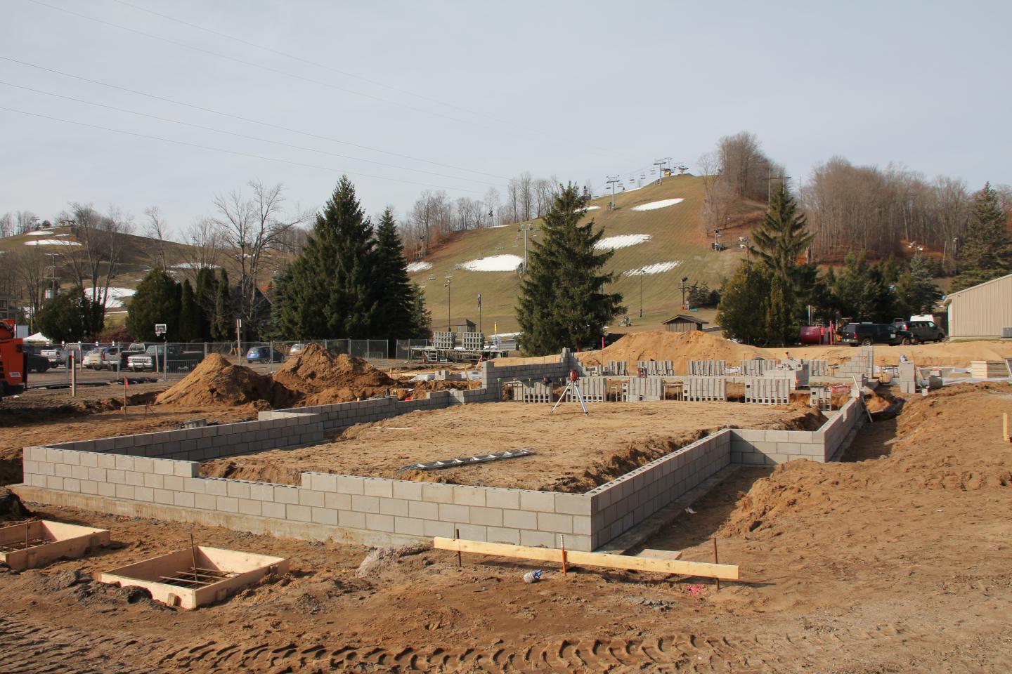 Construction site with brick foundation and grassy hill in the background.