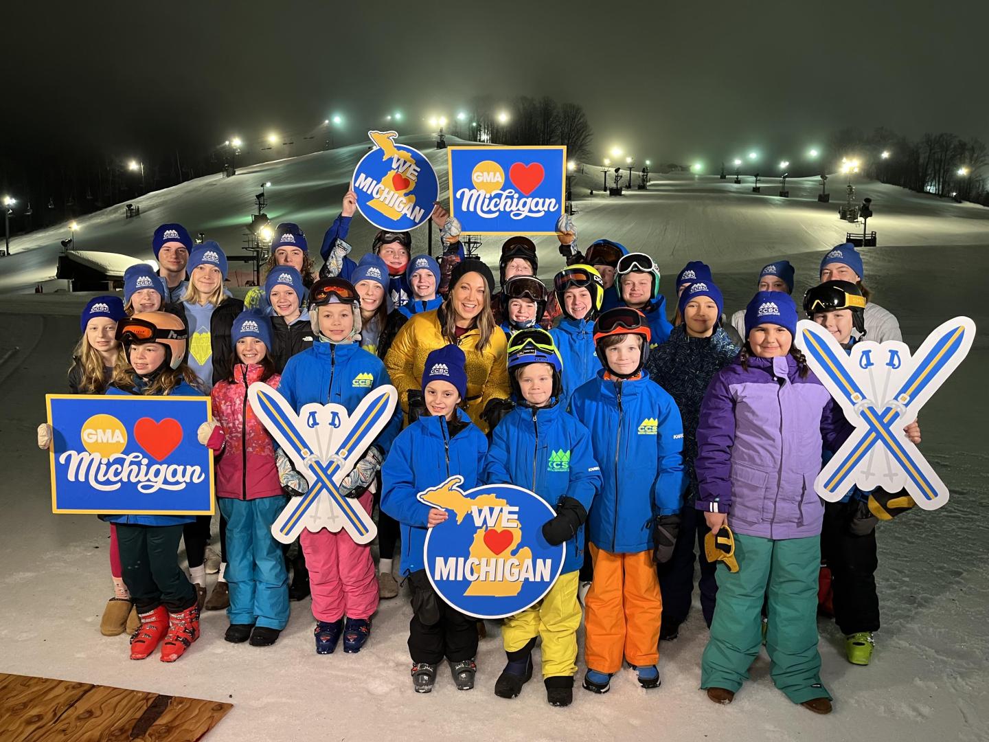 Group of people in winter clothing on a ski slope at night, holding "Pure Michigan" signs.