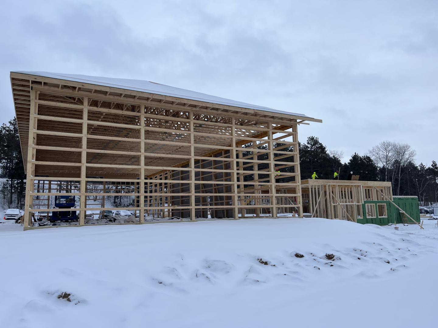Wooden building frame under construction, snow-covered ground, cloudy sky.