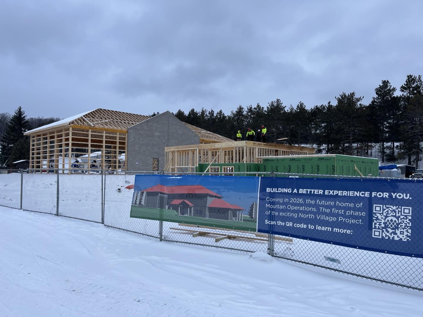 Building construction on snowy ground with a blue banner on a fence.