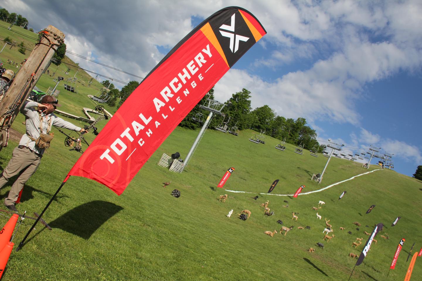 Archery event on a grassy hill under a blue sky with scattered clouds.