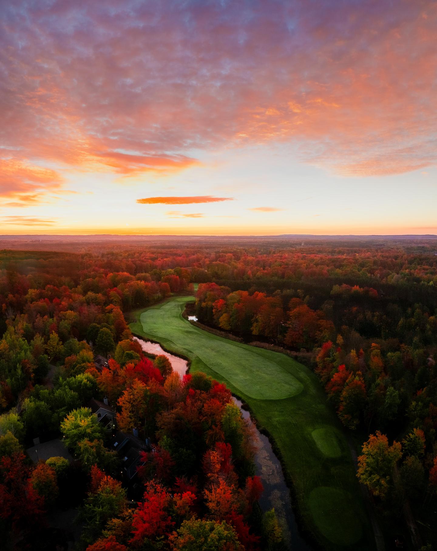 Sunset over a vibrant autumn forest with a winding green golf course.