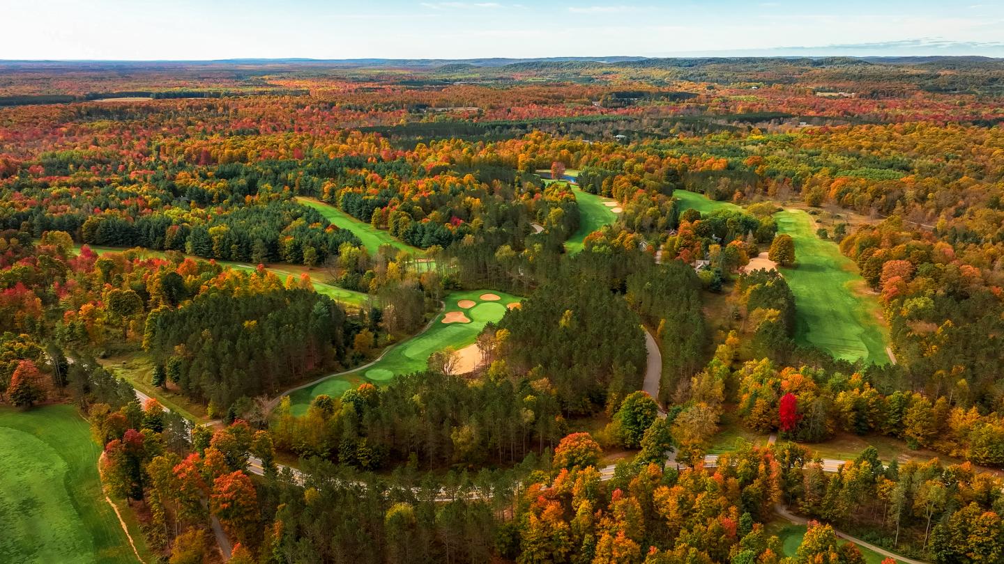 Aerial view of a golf course amid colorful autumn trees.