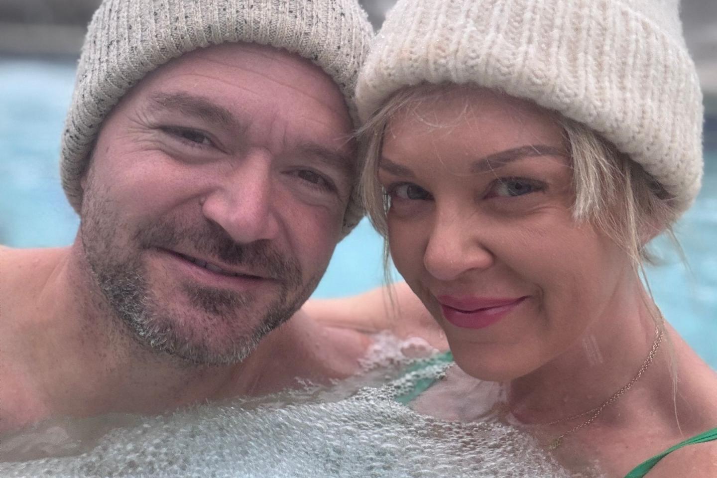 Two people in knit hats smiling in a hot tub.
