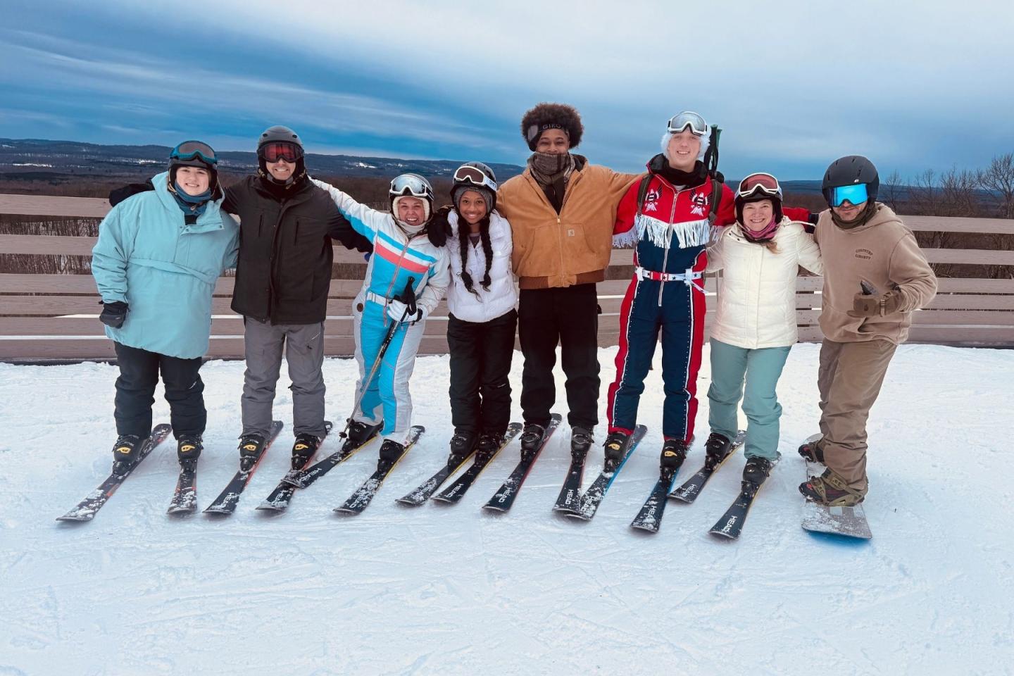 Group of seven friends smiling on a snowy ski slope.