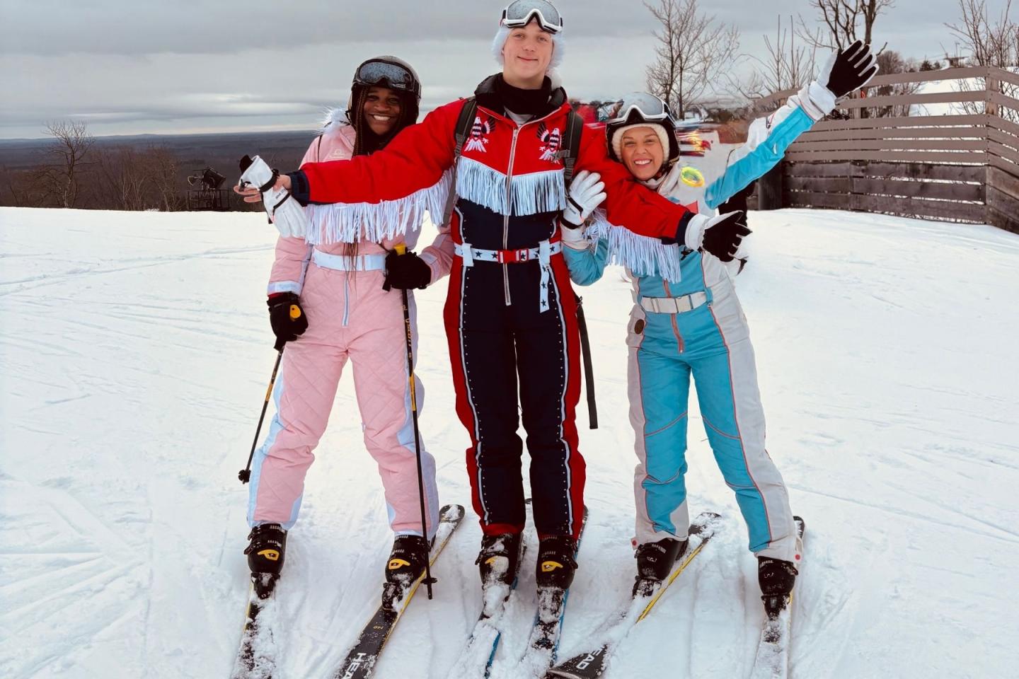 Three friends in retro ski outfits posing joyfully on a snowy slope.