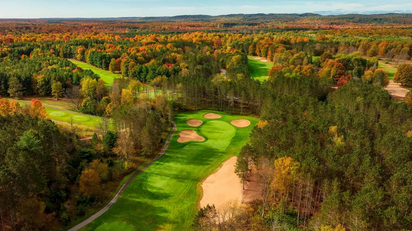 Aerial view of a golf course surrounded by autumn-colored trees.