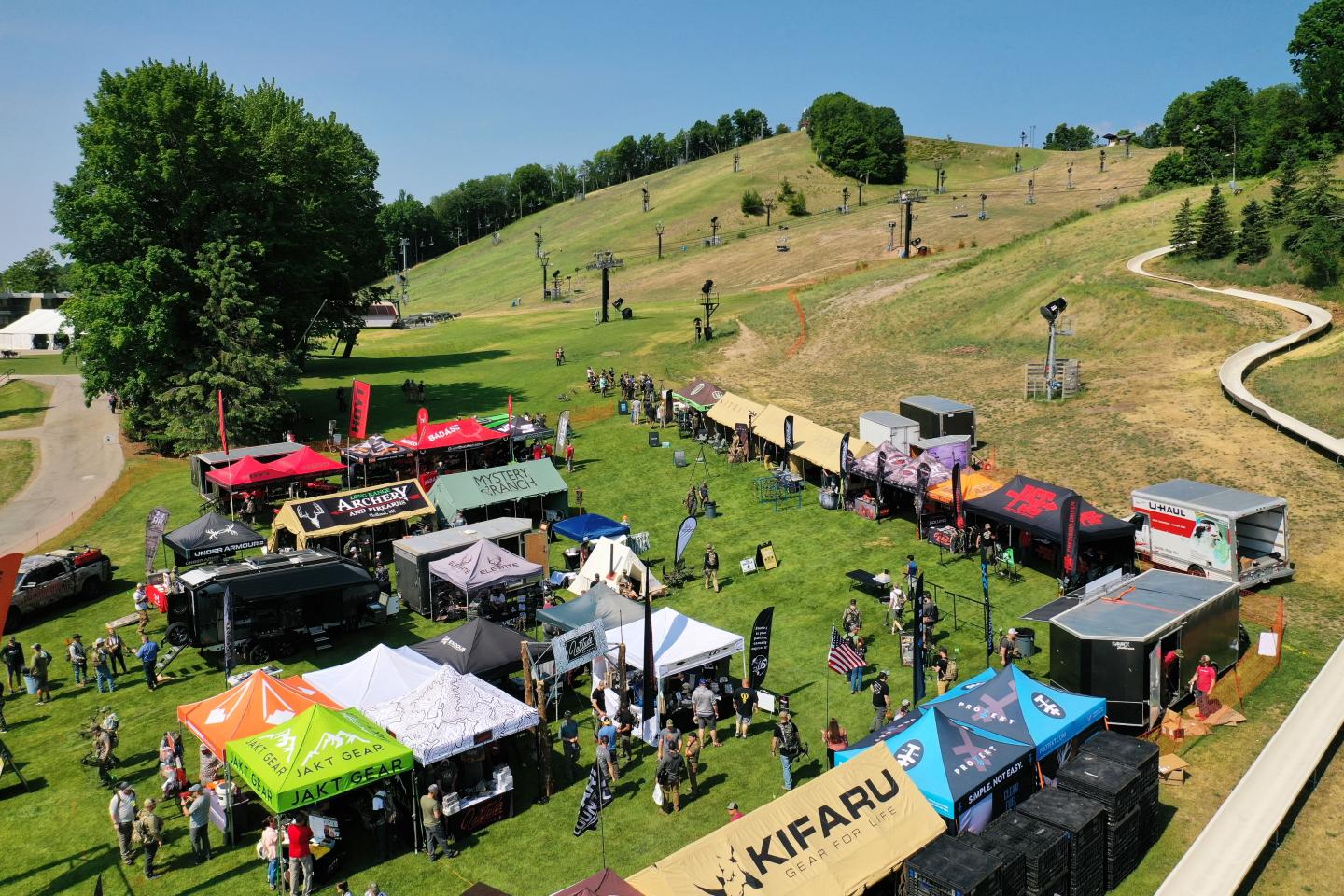 Outdoor festival with colorful tents on a grassy hillside.