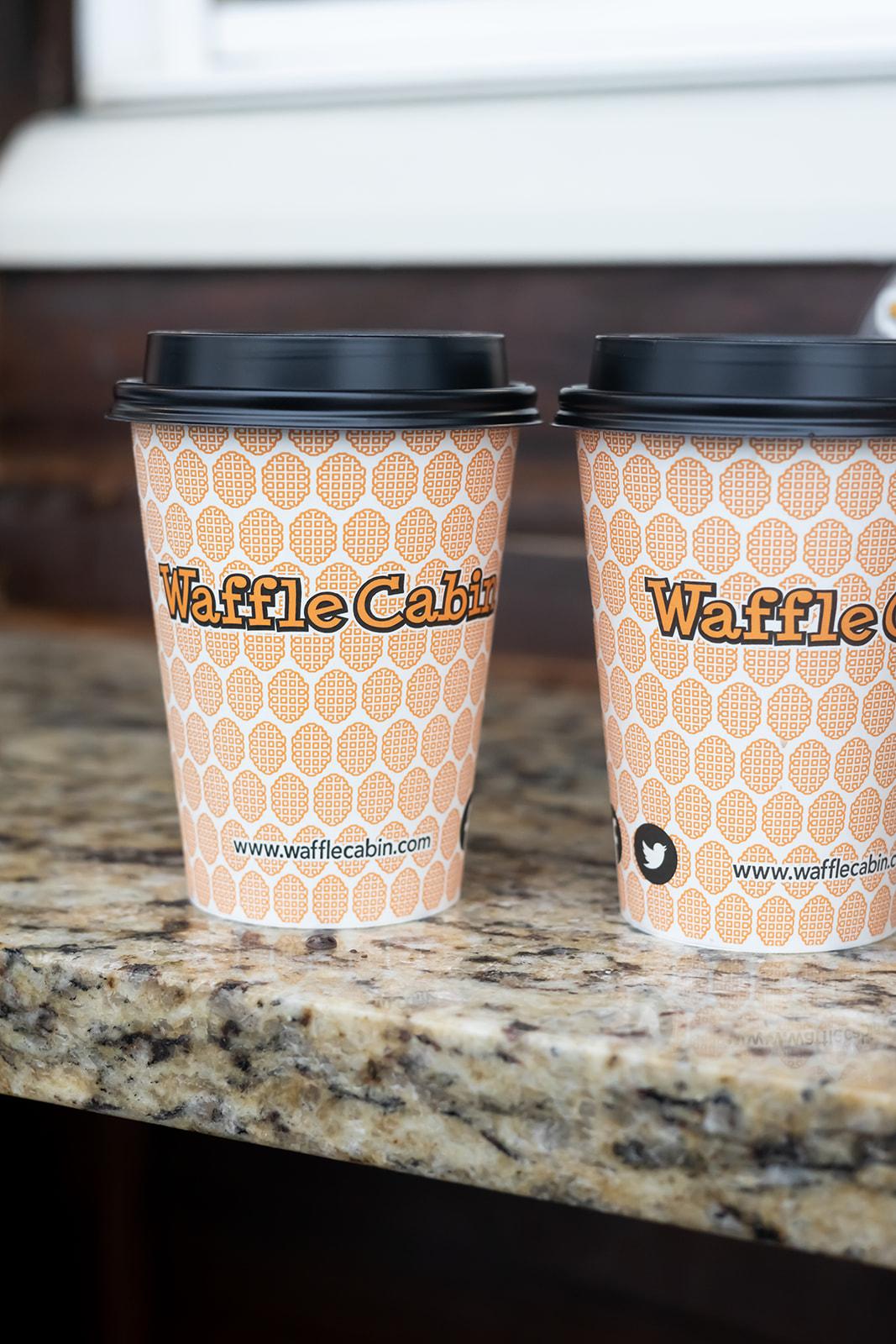 Two coffee cups with black lids on a granite countertop.