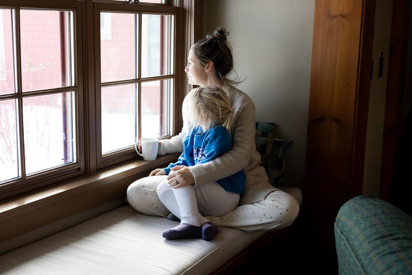 Woman and child sit on a window seat, gazing outside.
