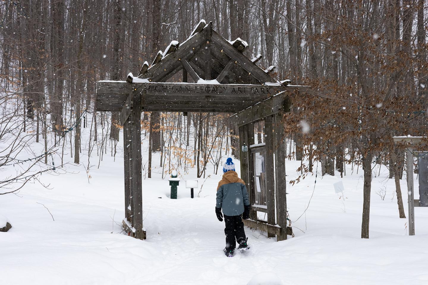 Child walks through snowy forest archway in winter clothing.