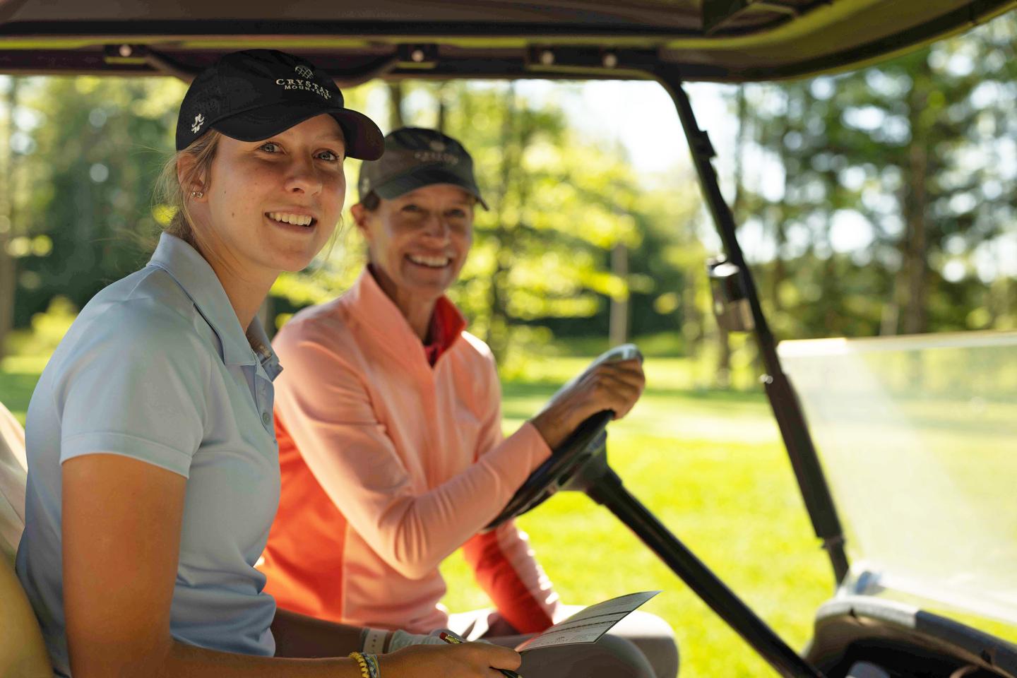 Two women smiling in a golf cart on a sunny day.