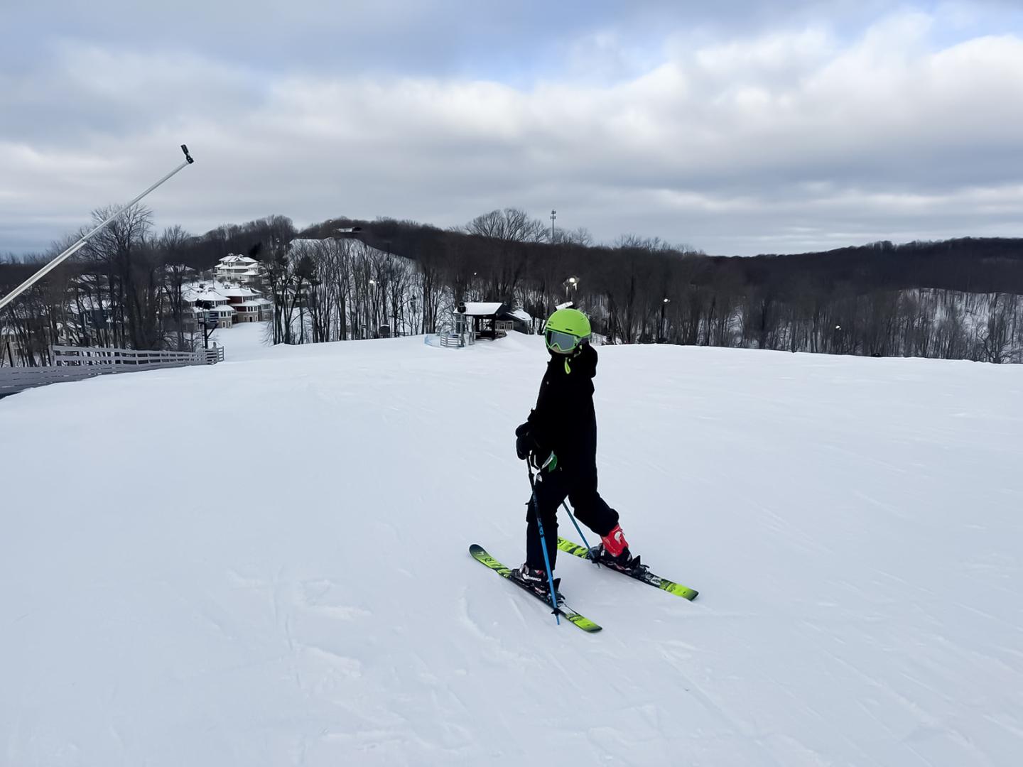 Skier in black jacket on snowy slope, overcast sky above.