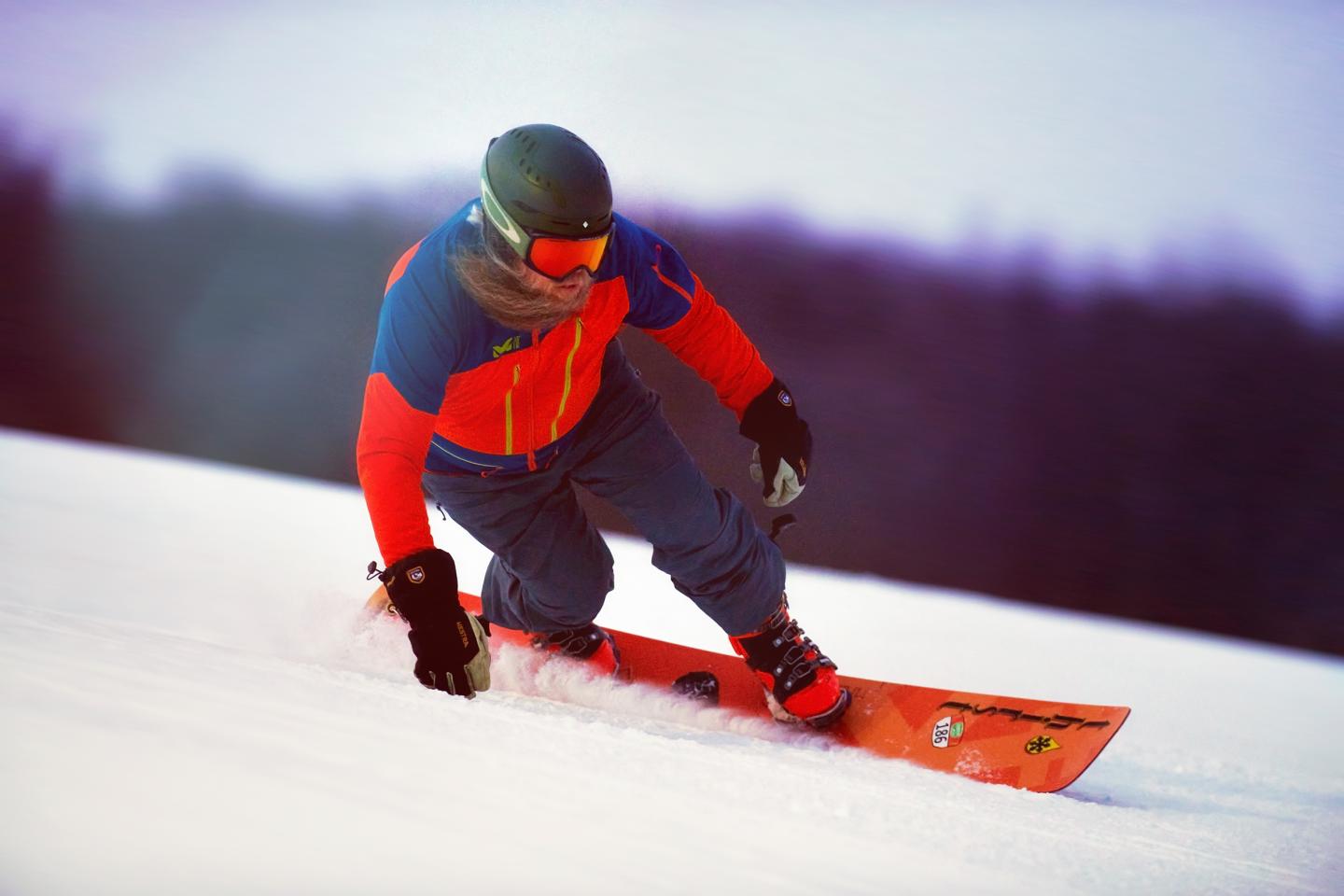 Snowboarder in red and blue gear carving down a snowy slope.