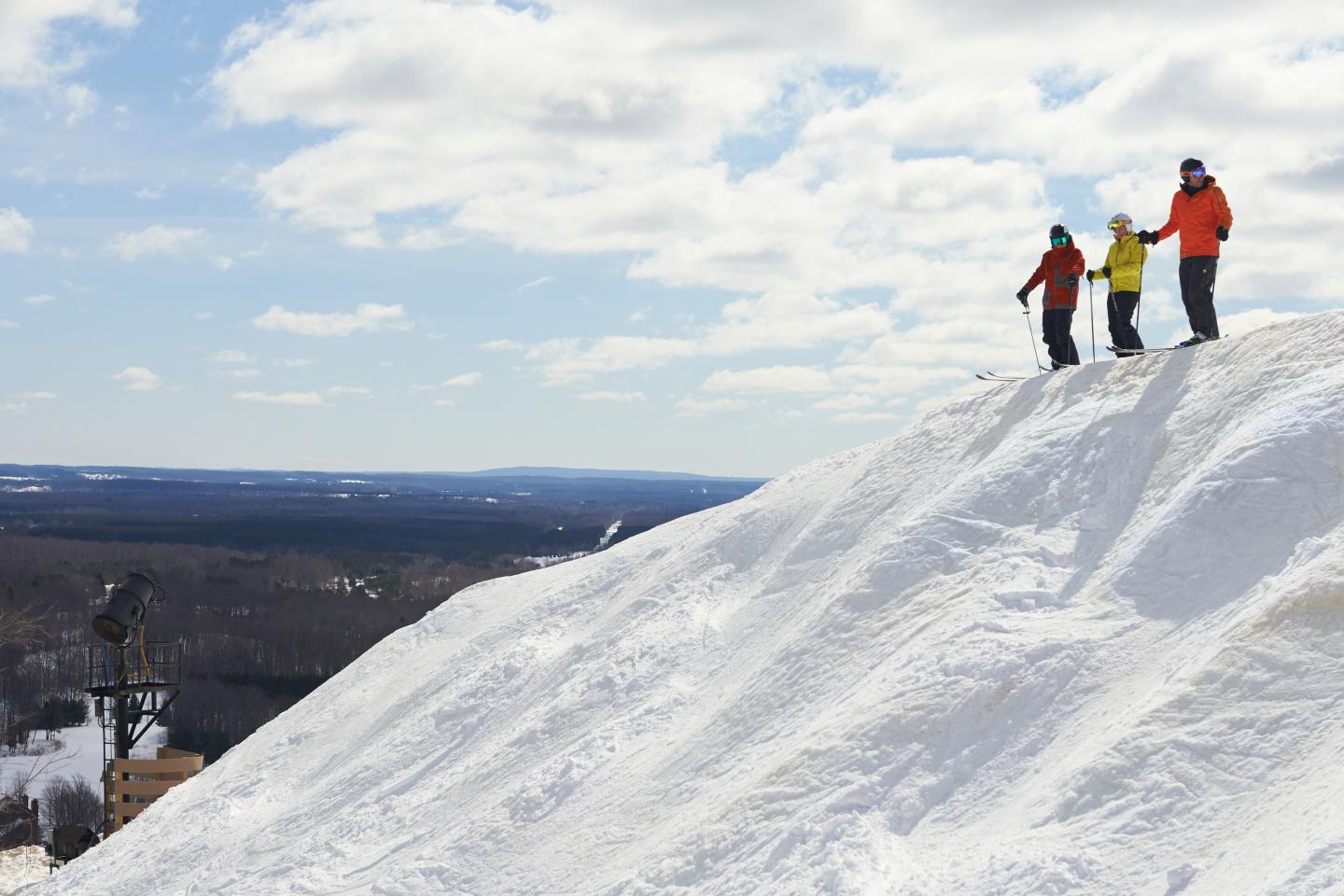 Three people stand on a snowy hill under a cloudy sky.