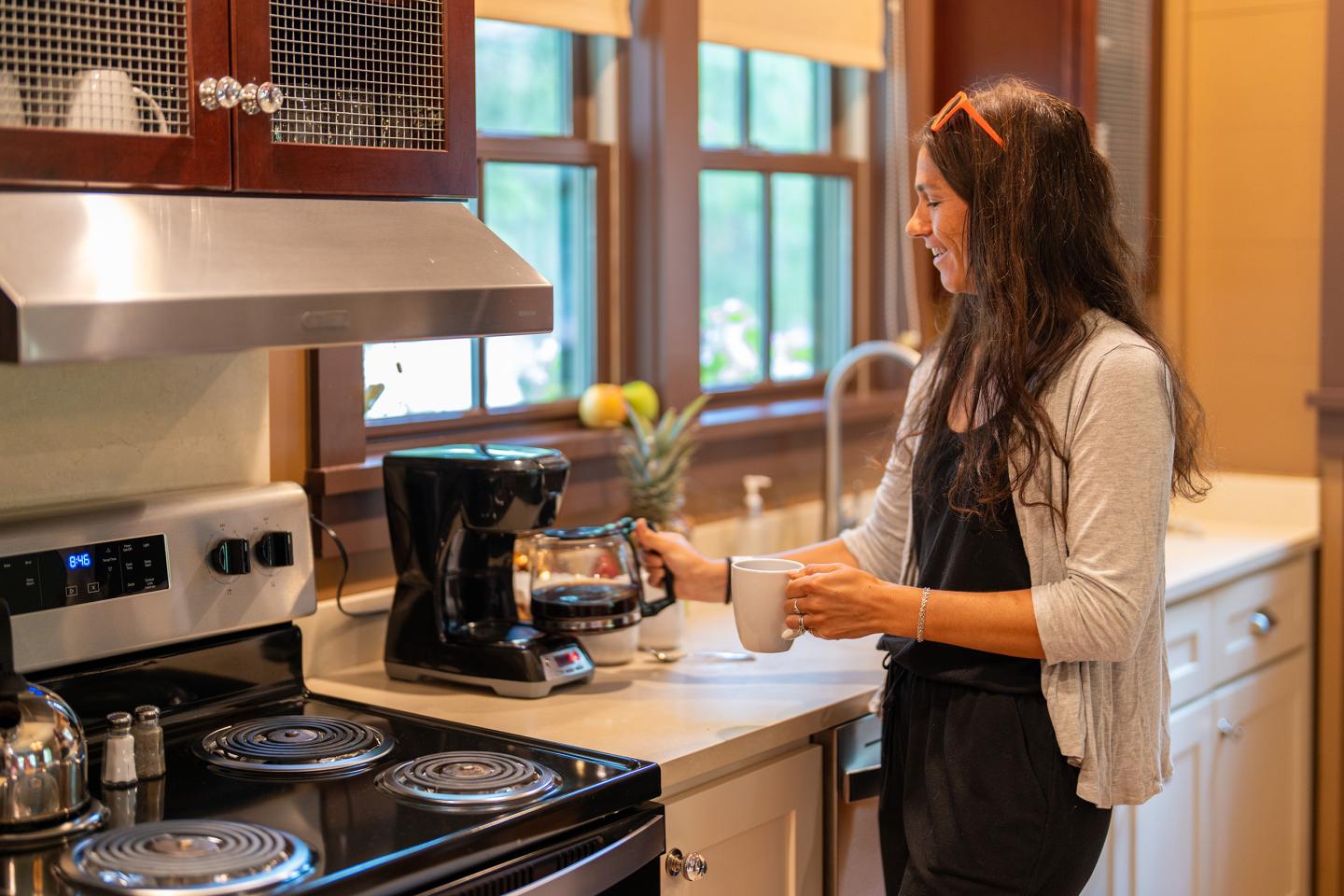 Woman in kitchen pouring coffee from a machine into a mug.