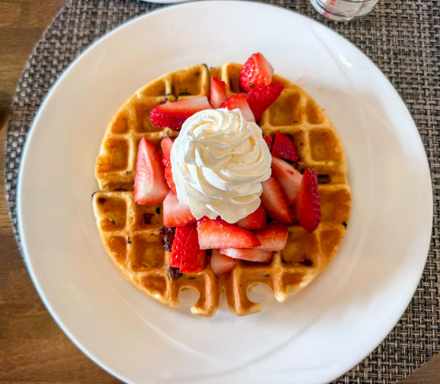 Waffle topped with whipped cream and strawberries on a white plate.
