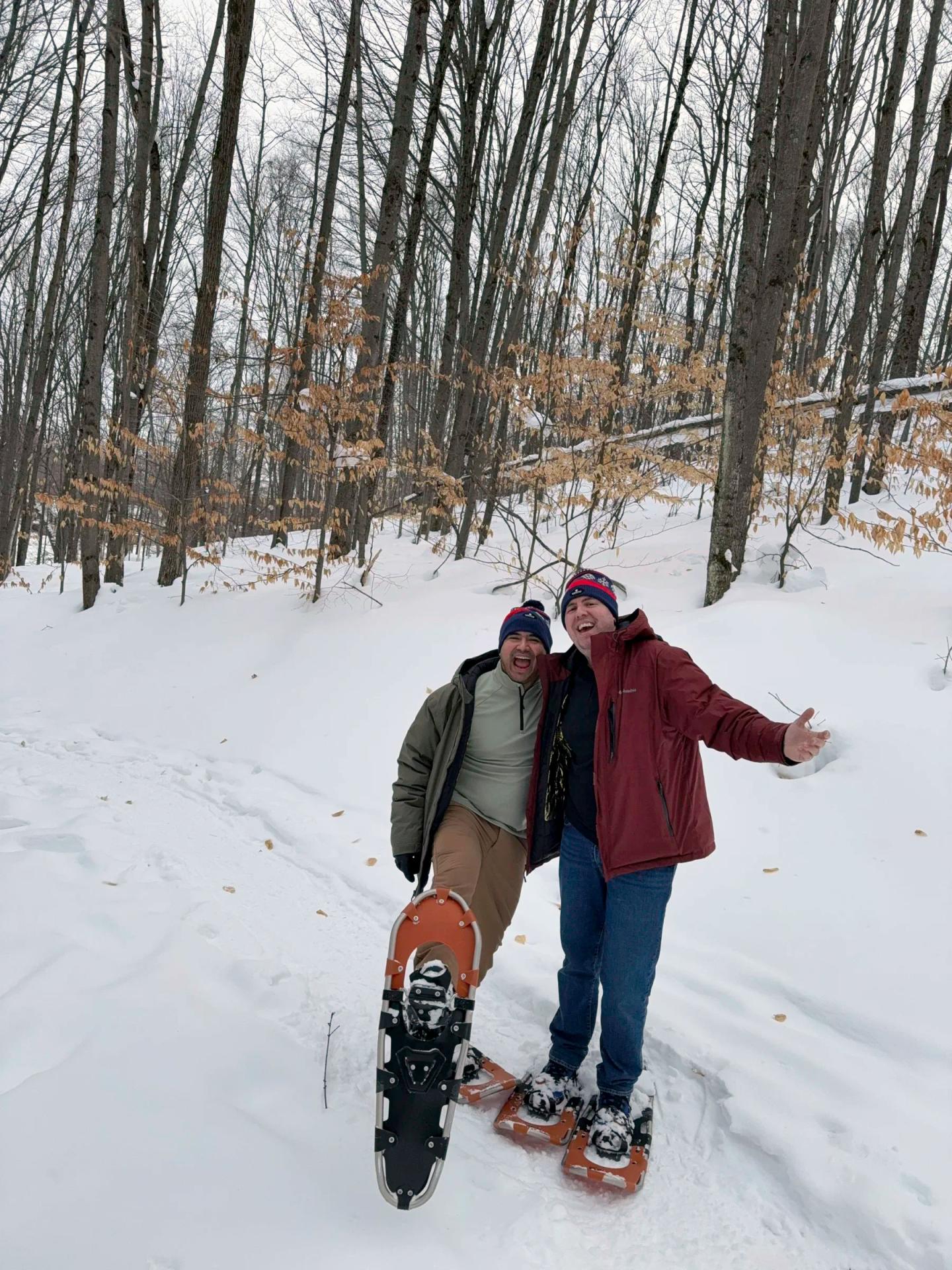 Two people wearing snowshoes, smiling in a snowy forest.