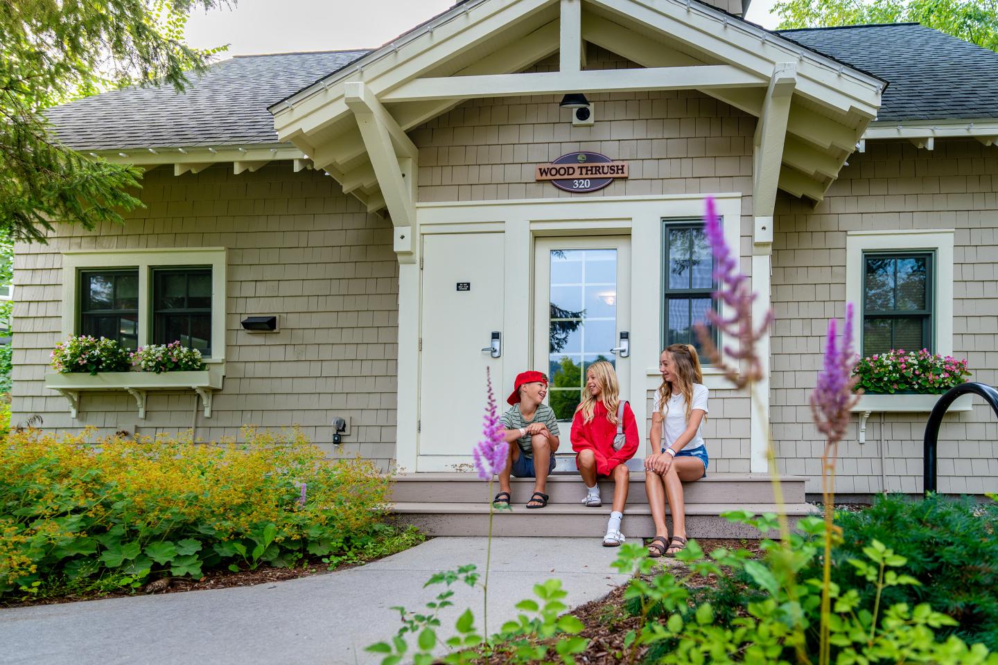 Children sitting and talking on steps of a charming cottage with a garden.