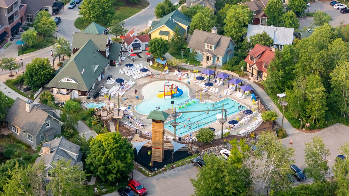 Aerial view of a colorful pool surrounded by trees and cozy buildings.