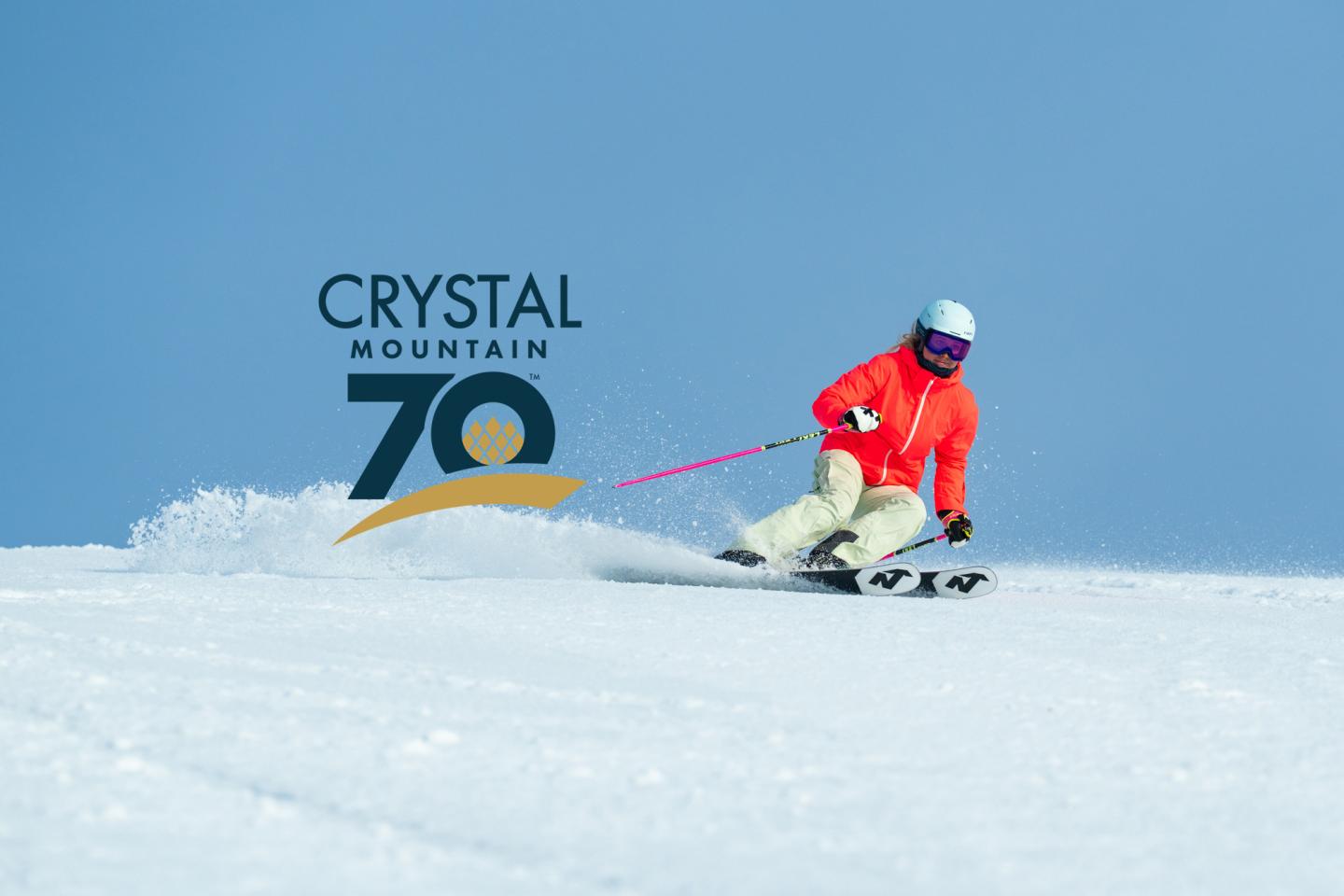 Skier in red on snowy slope against blue sky with Crystal Mountain 70th anniversary logo.