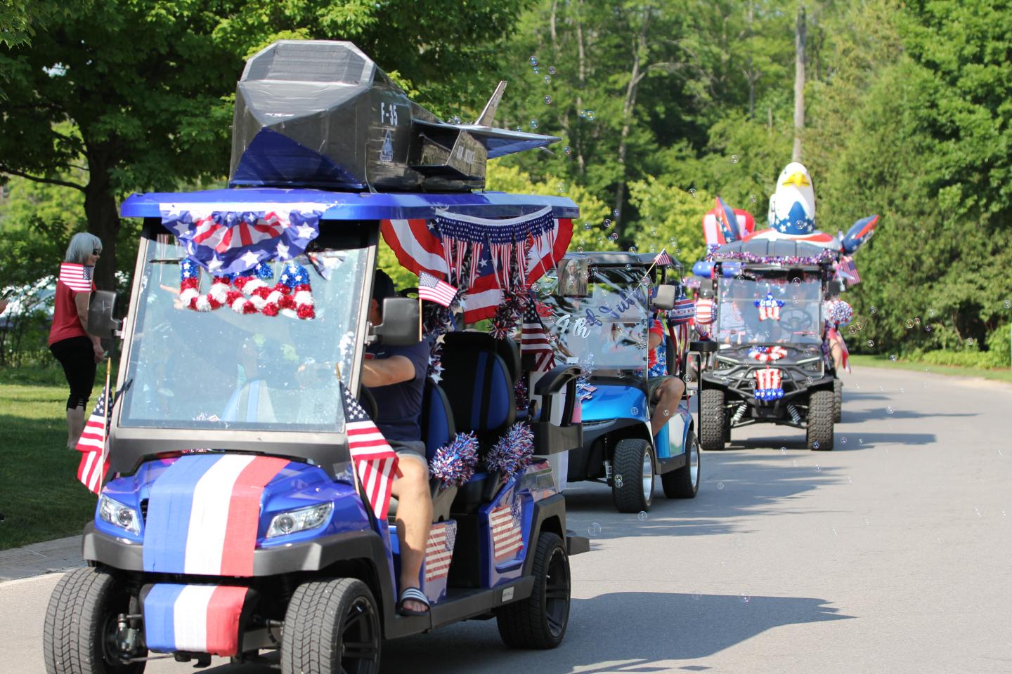 Parade of golf carts decorated with red, white, and blue on a tree-lined street.