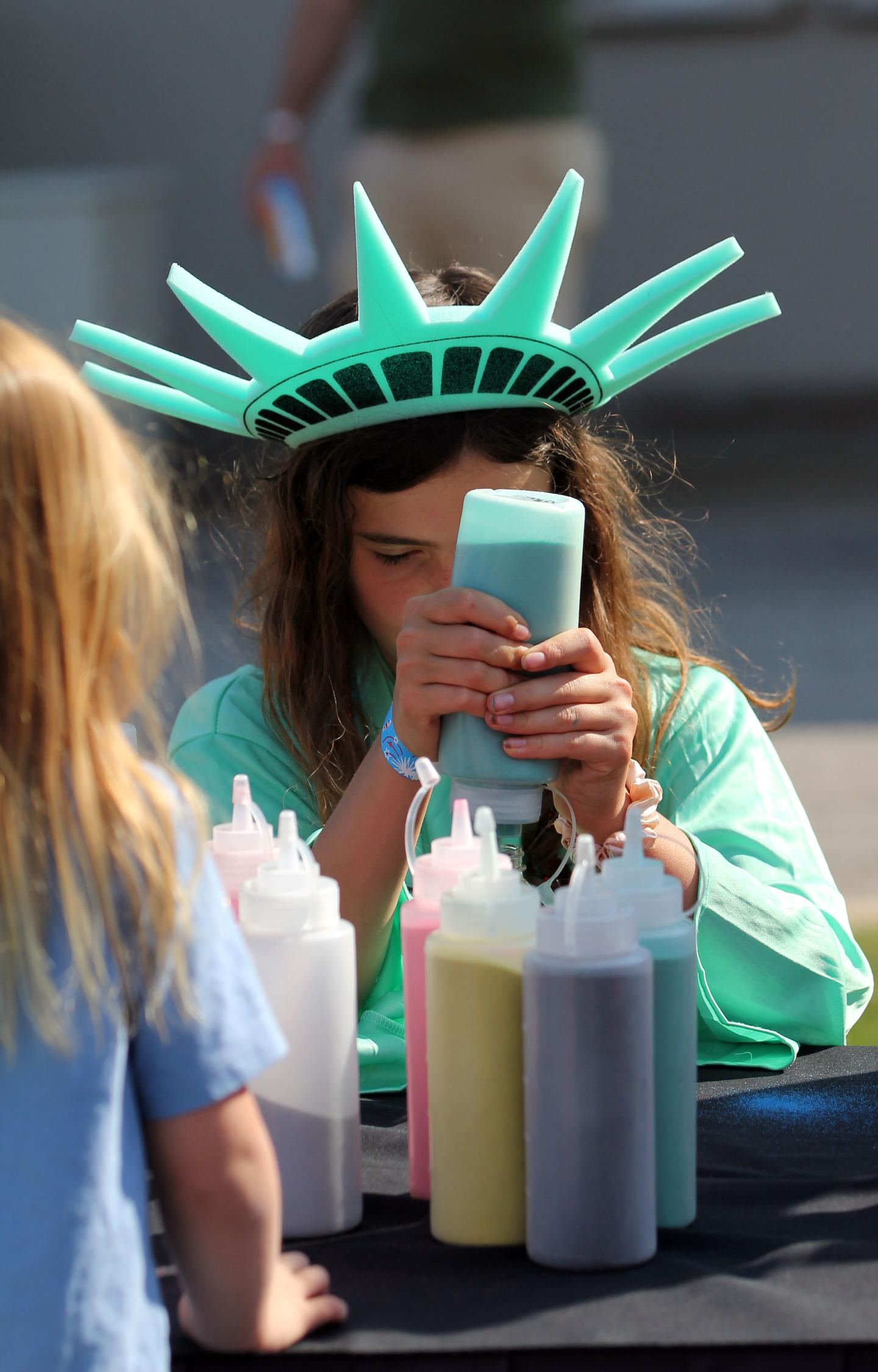 Child wearing Statue of Liberty crown focuses on squirting sand from bottle.
