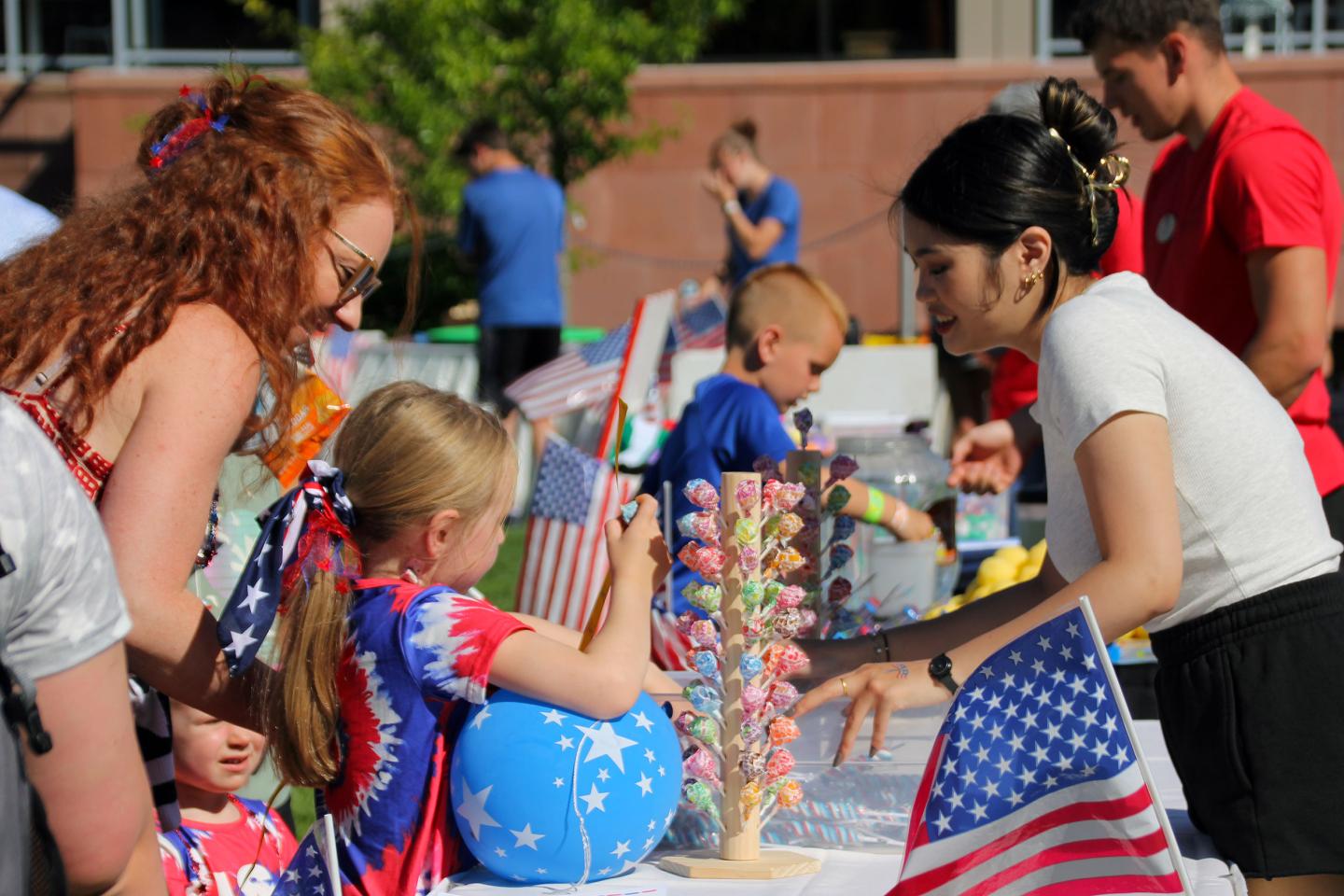 Children and adults at an outdoor table with flags and crafts.