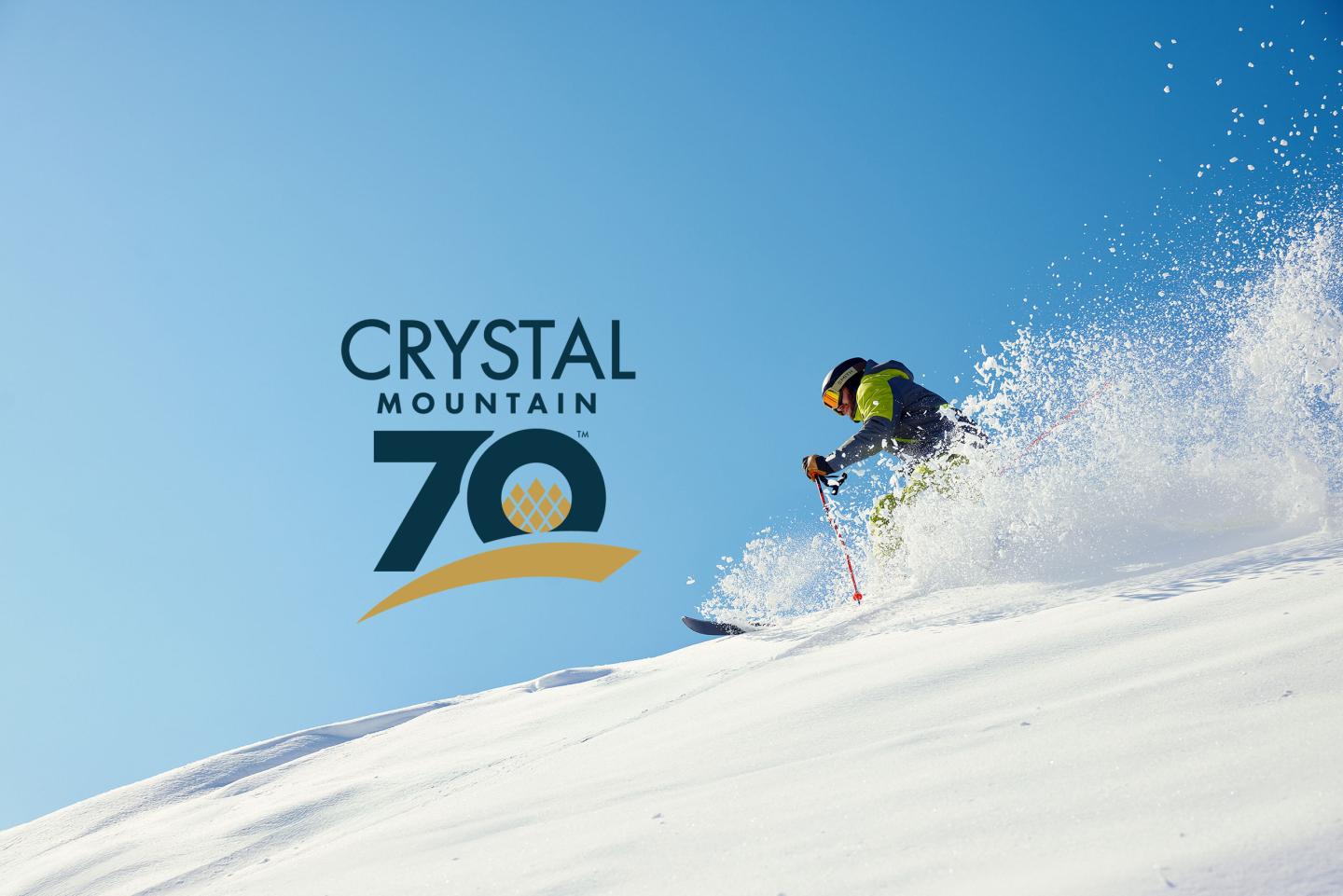 Skier in action on snowy slope under clear blue sky; "Crystal Mountain 70th anniversary" logo.