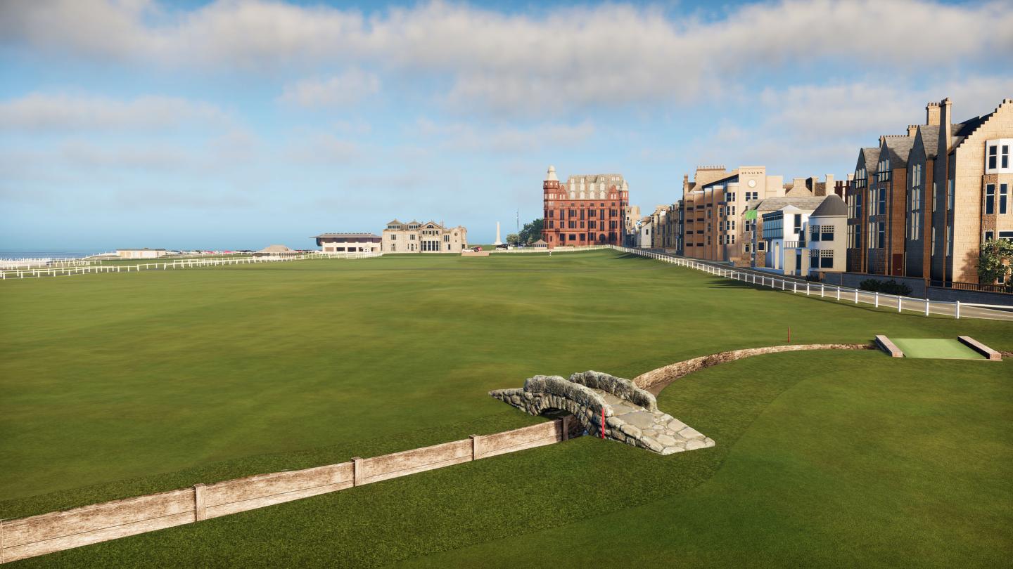 Wide green golf course with a stone bridge, buildings in the background under a blue sky.